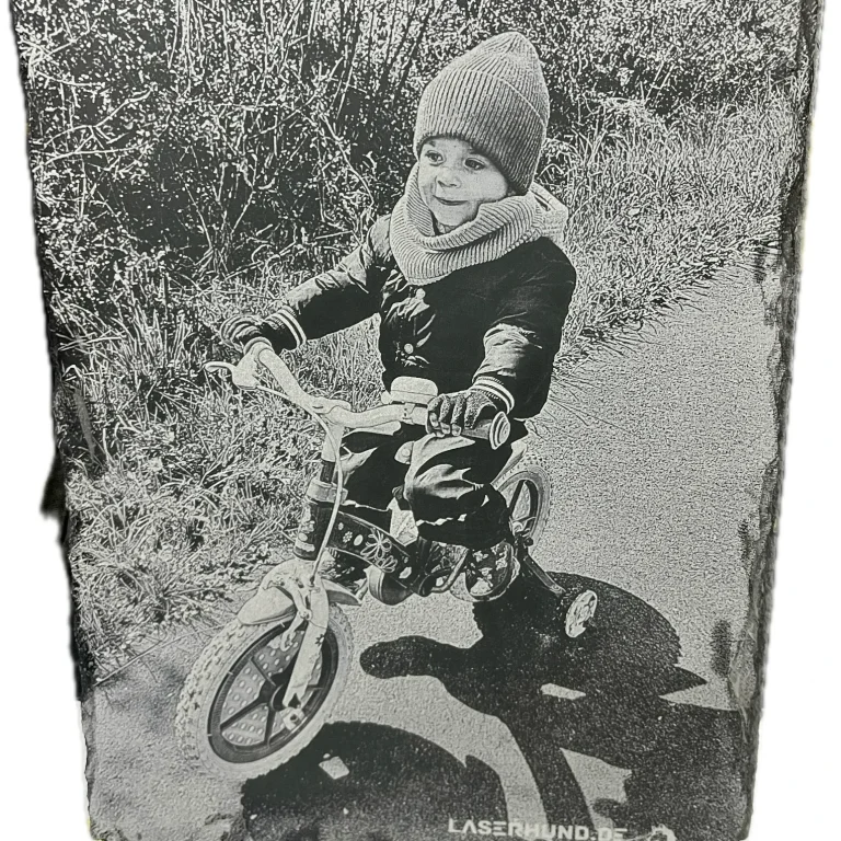 Lasergravur auf Schiefertafel Porträt Lasergravur auf Schiefer Junge mit Mütze und Schal fährt auf einem kleinen Fahrrad auf einem Weg.